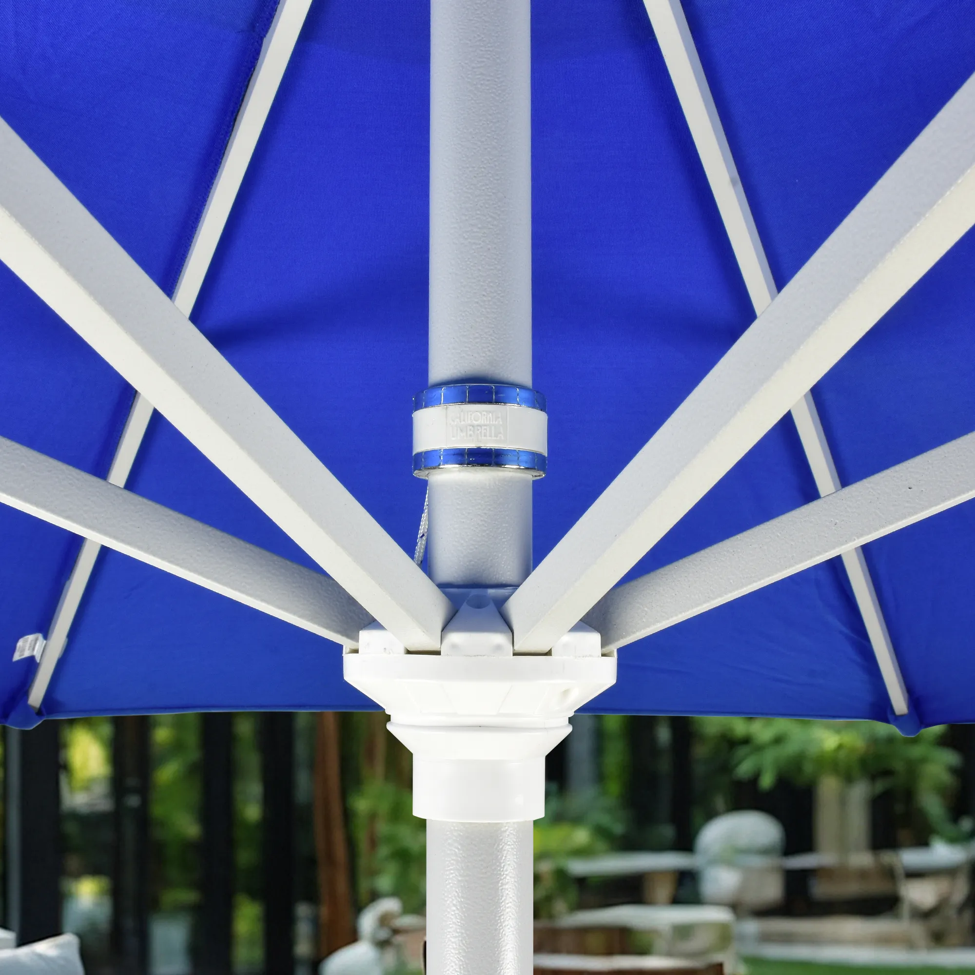 Close-up image of the durable aluminum center pole of the Pacific Trail Series Patio Umbrella by California Umbrella, clad in Sunbrella Pacific Blue fabric. This image highlights the robust construction and innovative design of the pole, which is built to provide stability and longevity under diverse outdoor conditions. The vibrant Pacific Blue Sunbrella canopy in the background contrasts sharply with the sleek white aluminum structure, emphasizing the umbrella's high-quality materials and craftsmanship, perfect for enhancing outdoor living spaces with style and functionality.