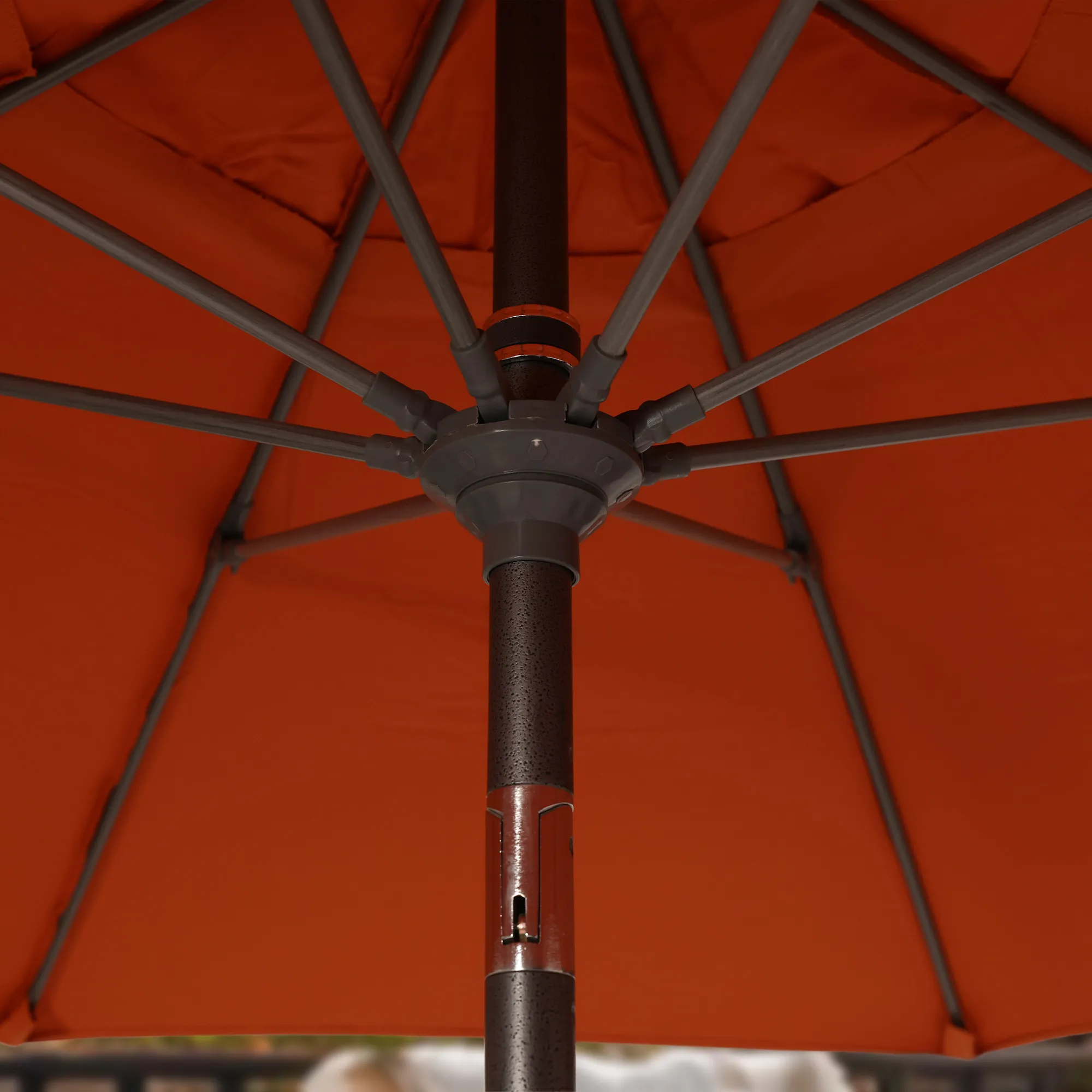 Close-up image of the durable aluminum center pole of the Sun Master Series Patio Umbrella by California Umbrella, set against a vibrant Sunbrella Tucson orange canopy. This photo highlights the robust construction and stylish design of the pole, equipped with a revolutionary collar tilt mechanism for easy angle adjustment. The gray finish of the pole contrasts beautifully with the bright fabric, illustrating the umbrella's functionality and aesthetic appeal suited for any outdoor setting